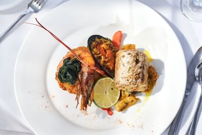 Plate with grilled fish, shrimp, and a colorful mix of sautéed vegetables at Bay Gardens Hotel