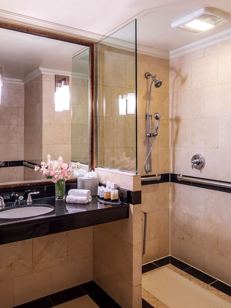 Granite vanity & inset sink, below framed mirror in tiled bathroom in Accessible On the Avenue Suite at Warwick New York