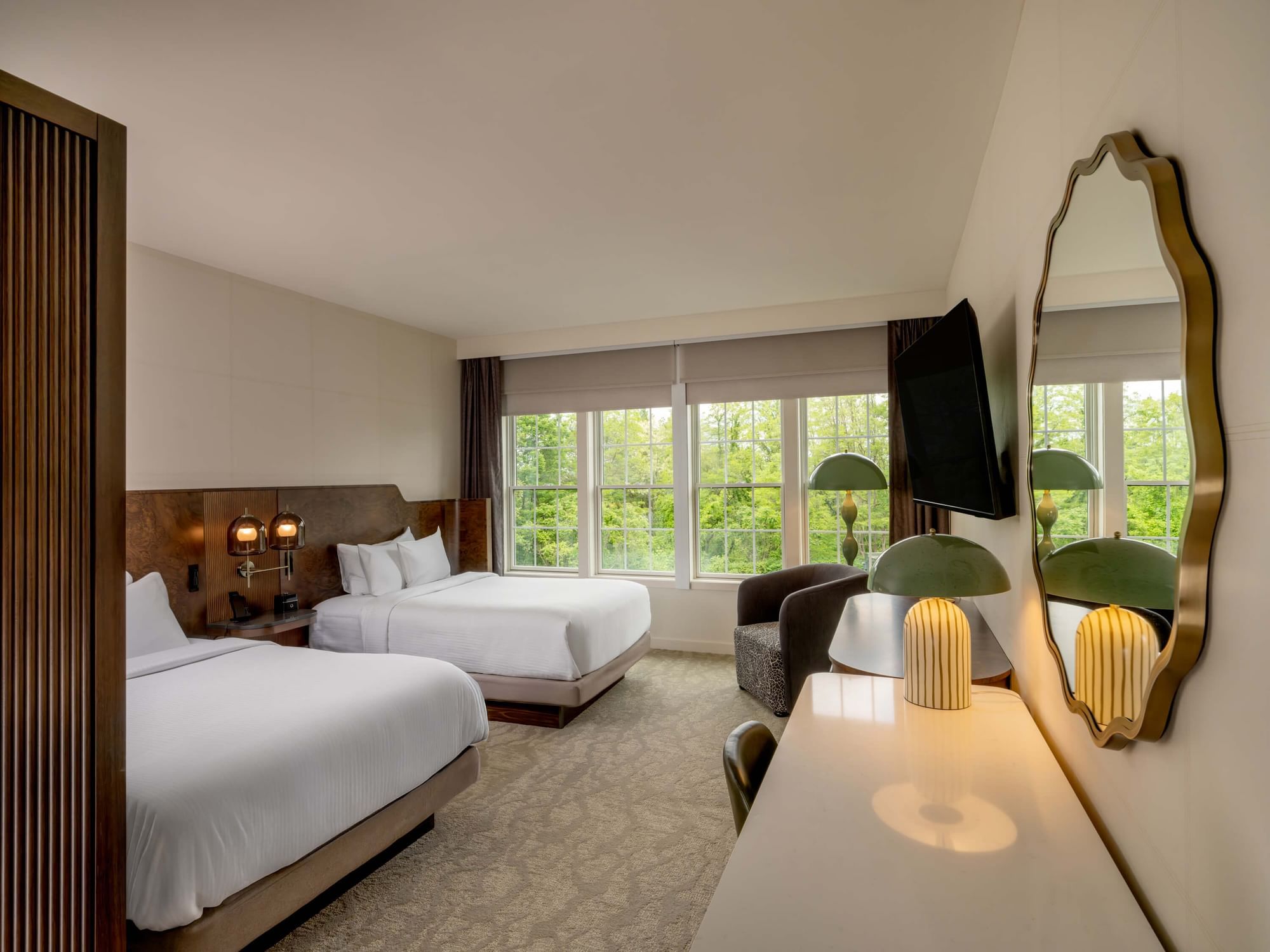 The sky double bed guest room with two beds, large windows, a desk, and a mirror reflecting a lamp and chair.