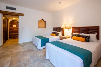 Two beds in a room with wooden headboards, white sheets, colorful pillows, and a tiled floor.