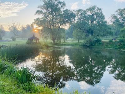 Wooden gazebo beside a calm pond reflecting trees during sunset on the grounds at La Tourelle Hotel and Spa