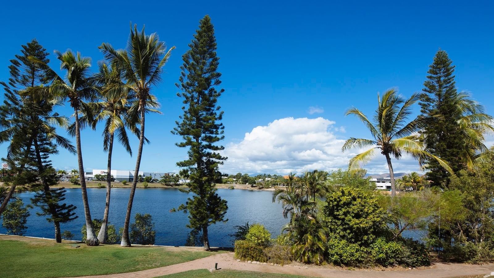 Serene lakeside view featuring palm trees, lush greenery, and a bright sky at Mercure Hotel Townsville