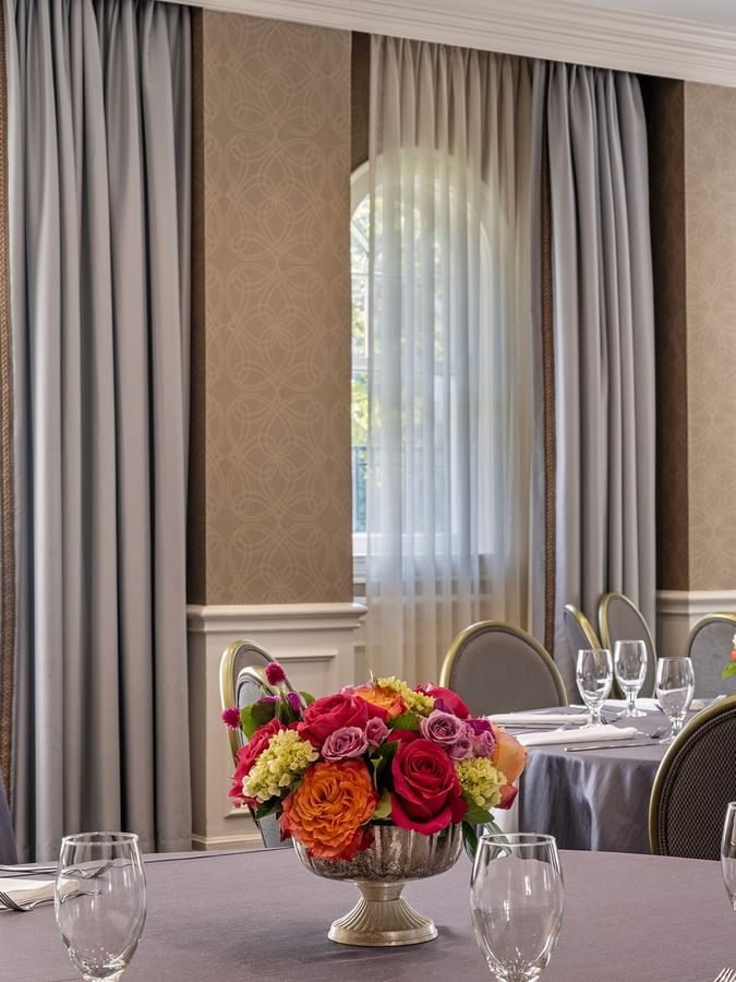 Round tables with floral centerpieces by grey curtains under soft window light in Oak Lawn/Terrace at Warwick Melrose Dallas