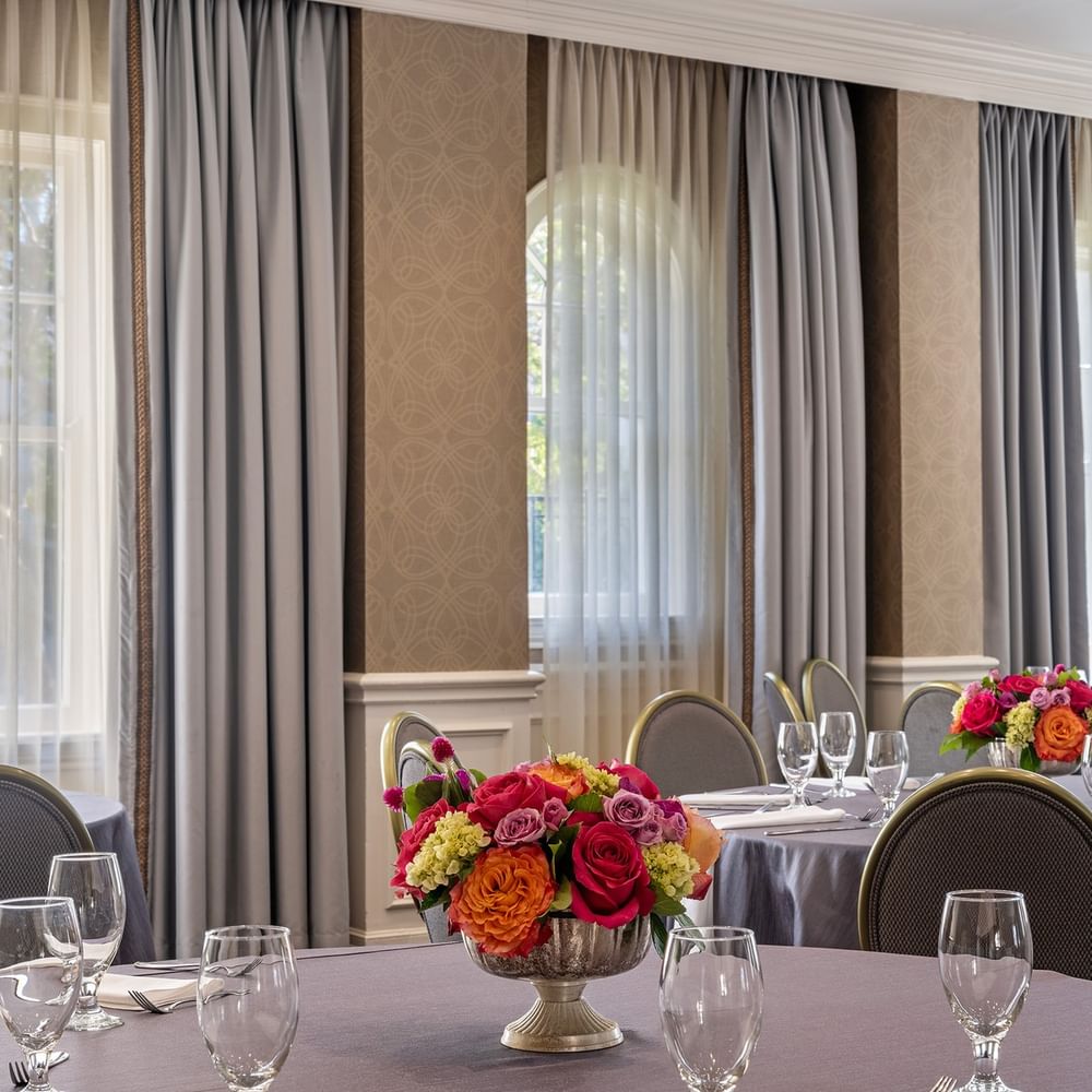 Round tables with floral centerpieces by grey curtains under soft window light in Oak Lawn/Terrace at Warwick Melrose Dallas