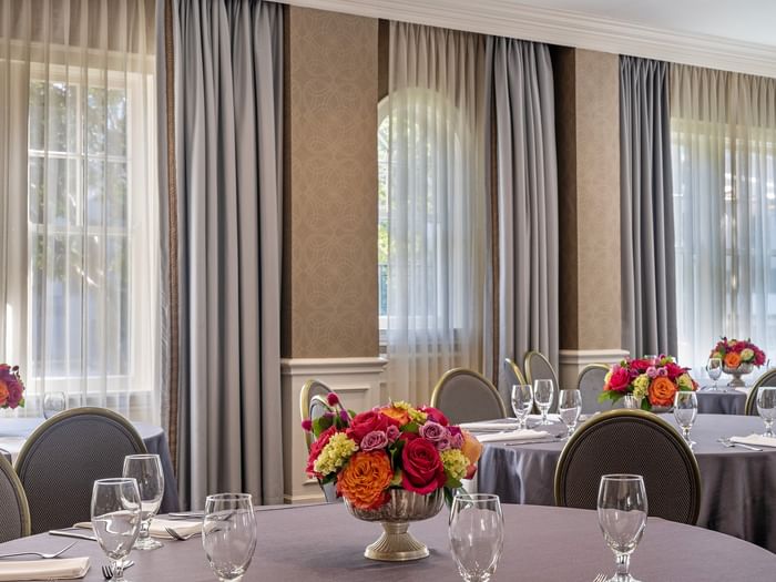 Round tables with floral centerpieces by grey curtains under soft window light in Oak Lawn/Terrace at Warwick Melrose Dallas