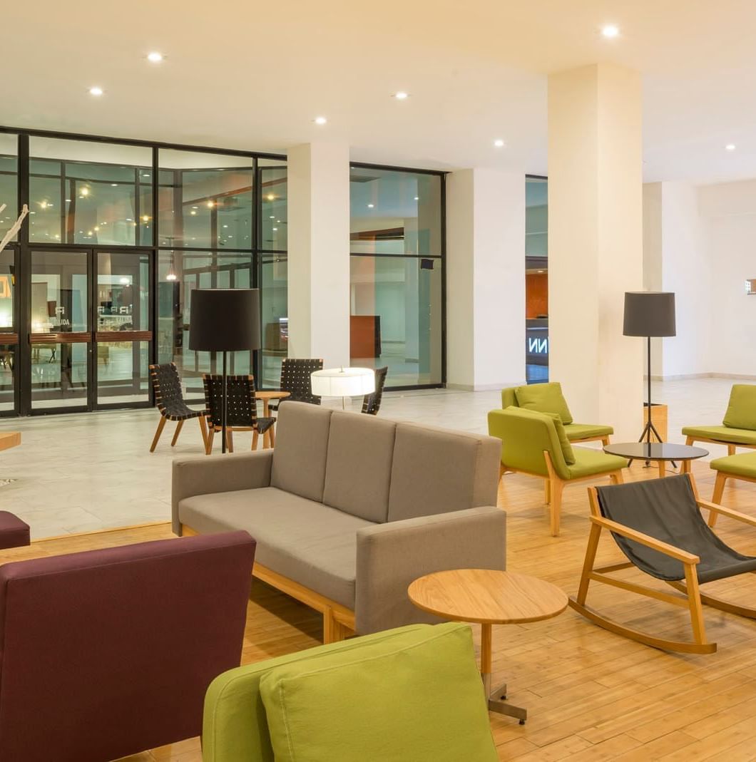 Plush green and purple chairs by a rocking chair surrounding wooden tables under tall pillars at Real Inn Mexicali