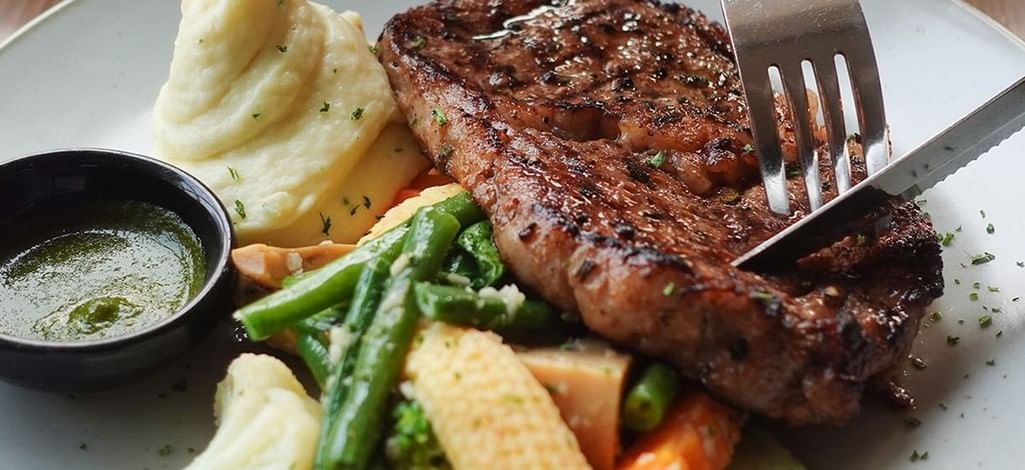 Grilled steak served with vegetables, roasted potatoes and sauce