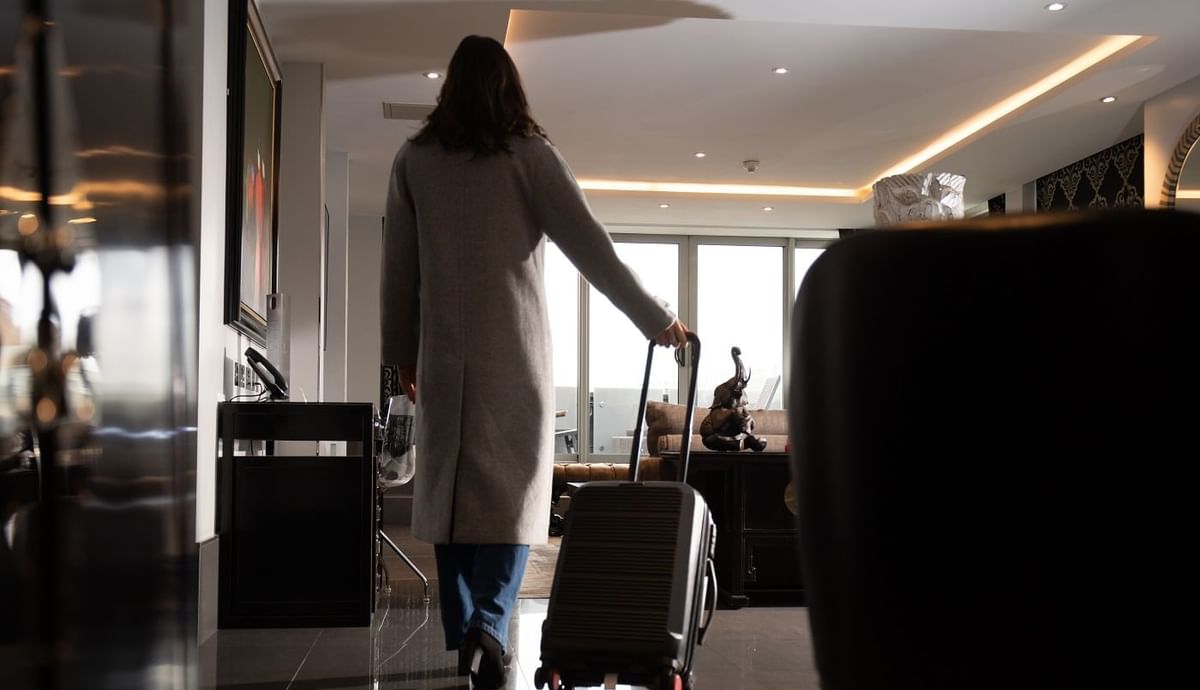 A guest in a sleek grey coat pulls luggage as she enters a modern luxury suite at The May Fair Hotel