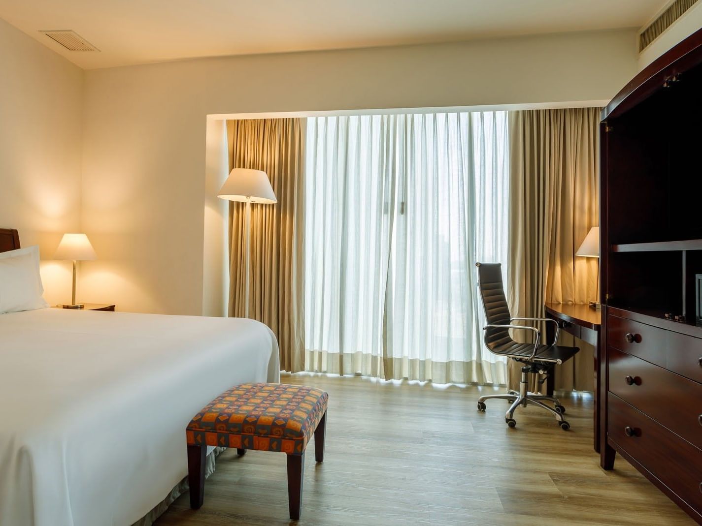 Spacious King Junior Suite at Camino Real Pachuca, with a large window, workspace, and a colorful patterned bed-end bench