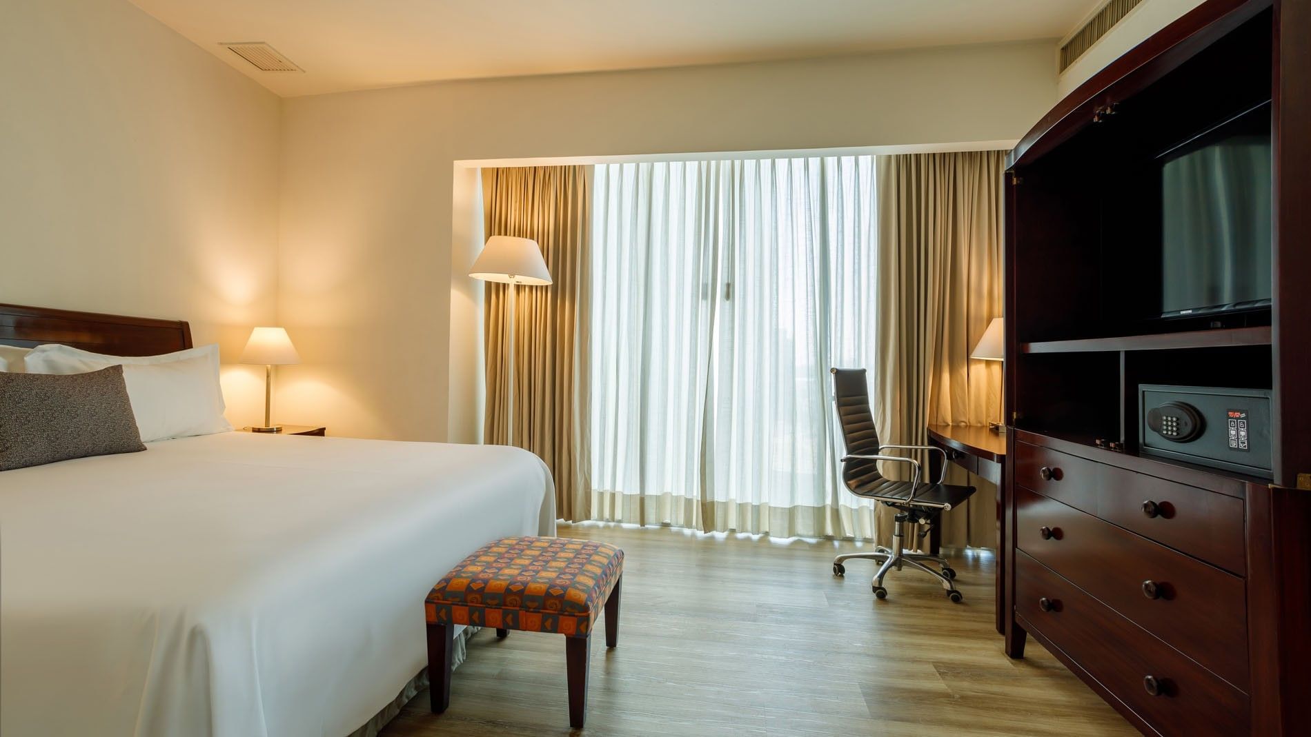 Spacious King Junior Suite at Camino Real Pachuca, with a large window, workspace, and a colorful patterned bed-end bench