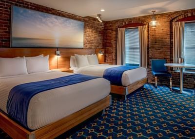 Two queen beds with sea art above the headboard and windows near a table in Double Queen City View at Harborside Inn Boston