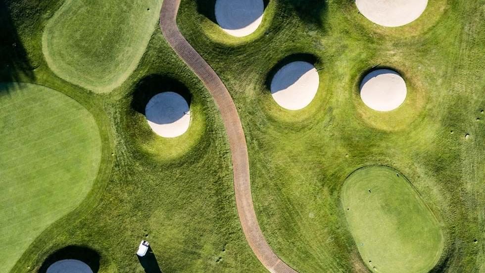 Aerial view of a golf course with multiple sand bunkers and a cart path at Falkensteiner Residences Edelweiss