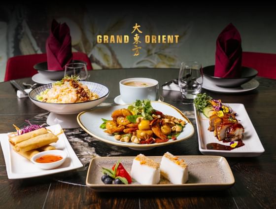 A dining table set with multiple plates of Asian cuisine, a bowl of soup, and two drinks. 