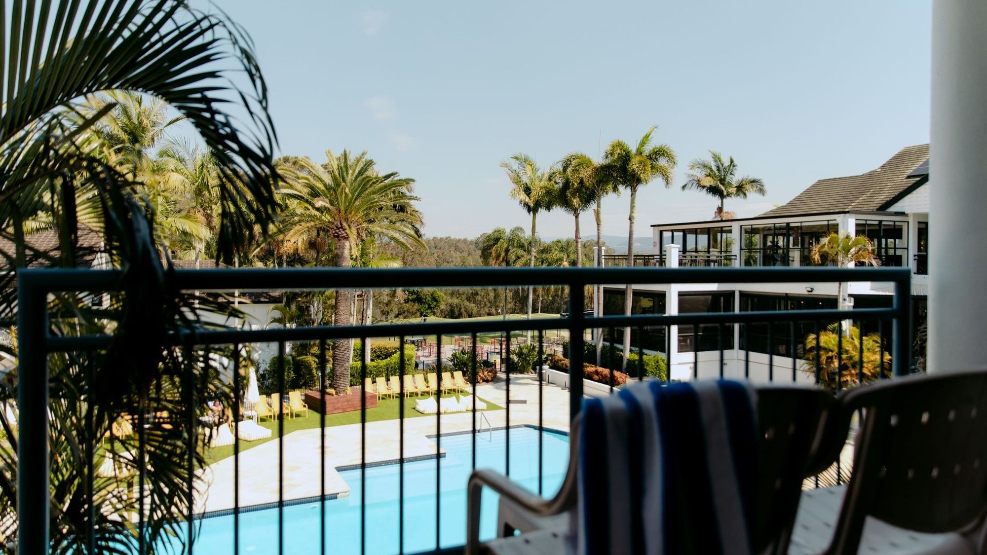 Balcony with chairs and a pool view under a clear blue sky.