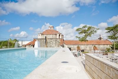 Pool reflecting bright sky, overlooking historic domed building and lush greenery at Billini Hotel Historic Luxury