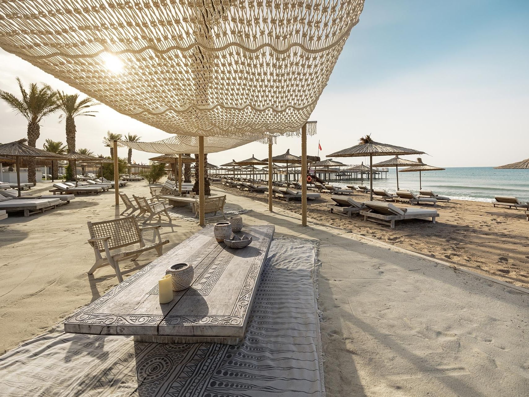 A beach with lounge chairs, tables, umbrellas, and a canopy Cullinan Belek.