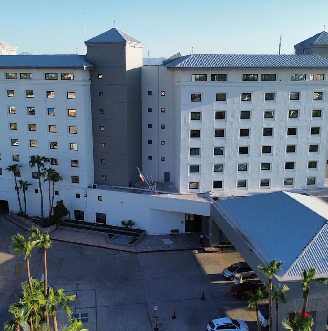 Aerial view of Real Inn Mexicali with palm trees by the entrance under a clear blue sky