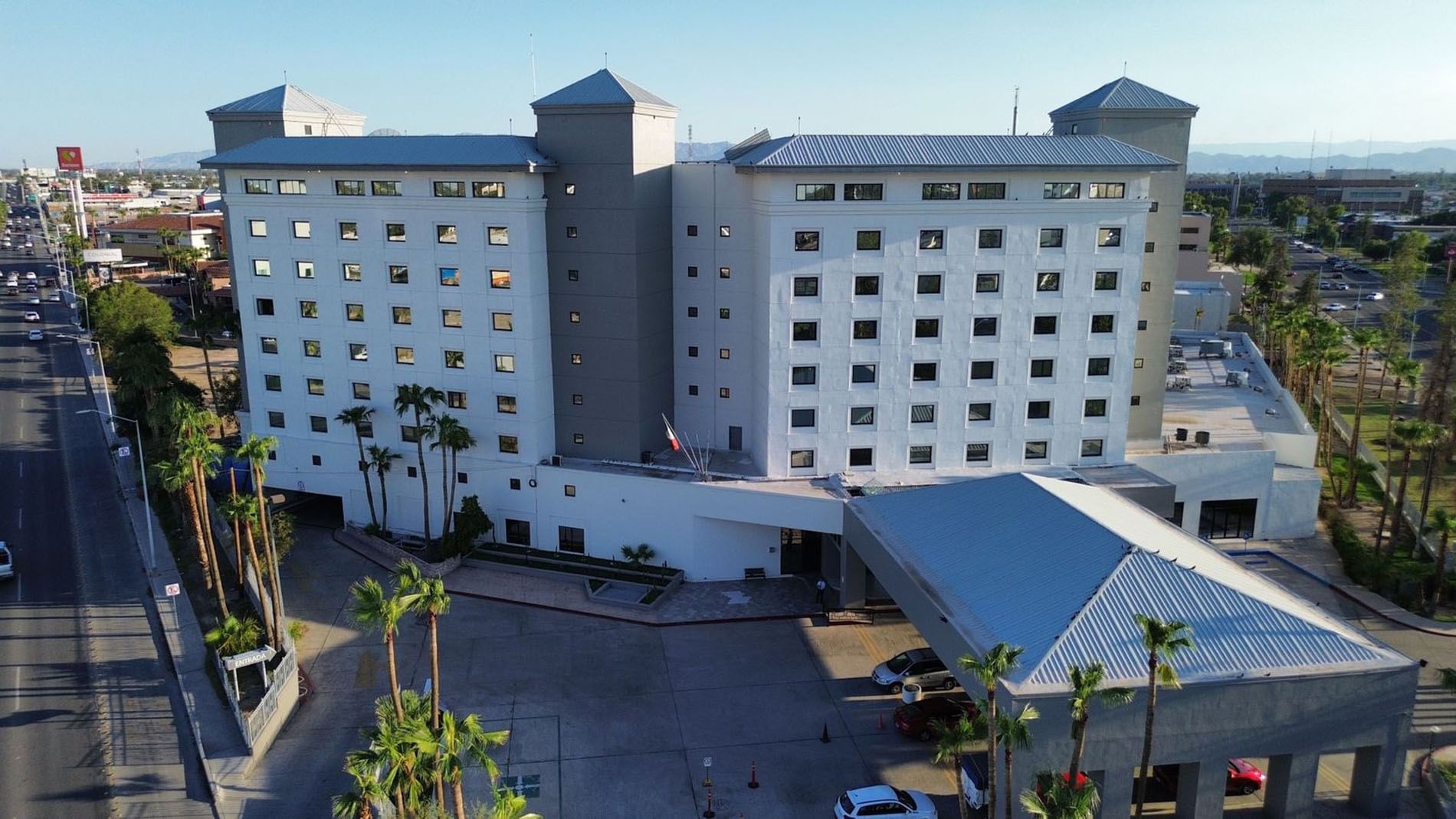 Aerial view of Real Inn Mexicali with palm trees by the entrance under a clear blue sky