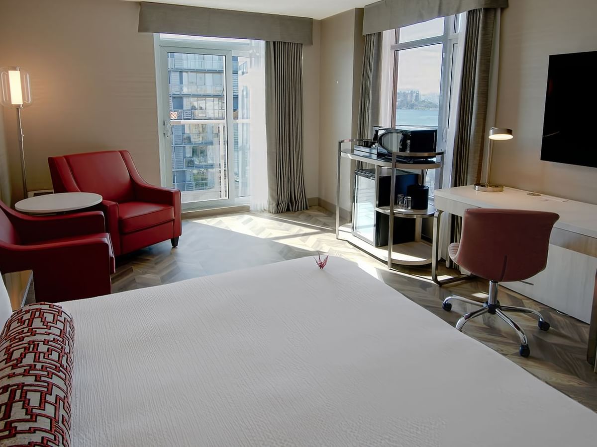 Hotel guestroom with king bed, window, TV, work desk, and two sofas.