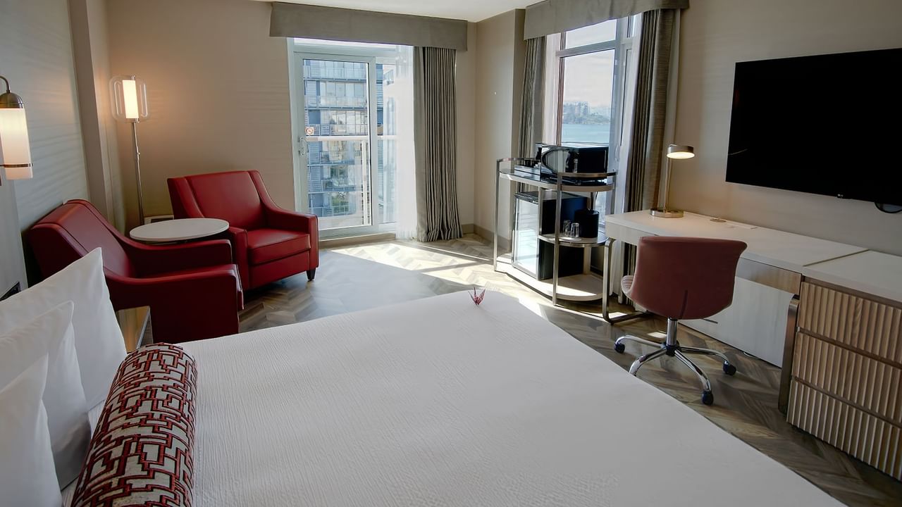 Hotel guestroom with king bed, window, TV, work desk, and two sofas.