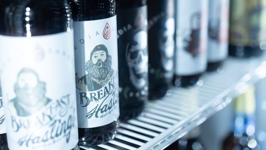 Row of craft beer bottles with illustrated Breakfast Hastings labels on a fridge shelf at Media Sangre in Araiza Calafia