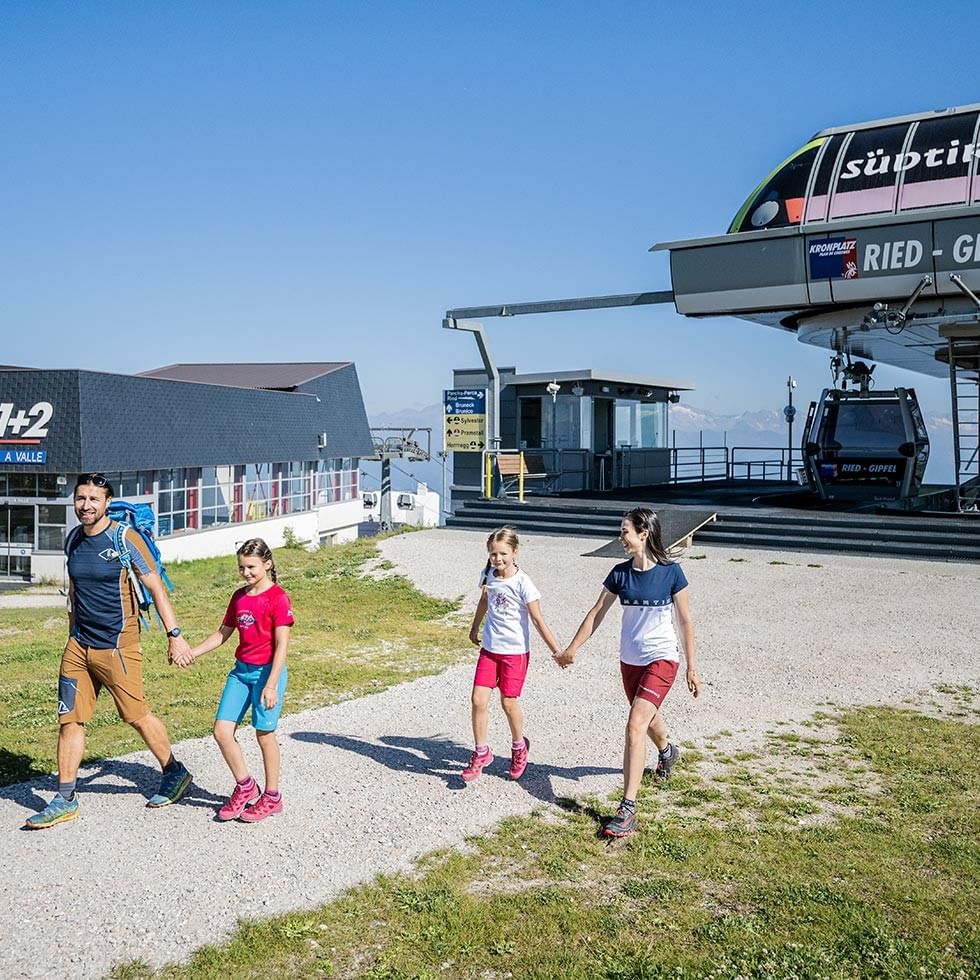 A family of four walking together holding hands in front of a ski lift station.
