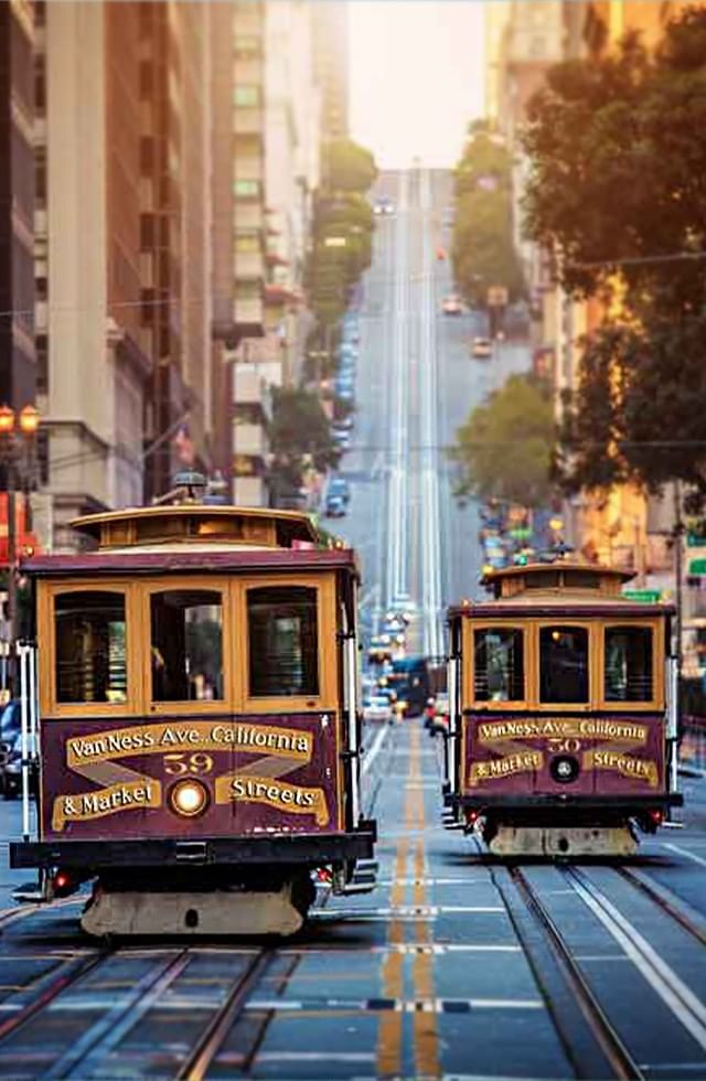 Two cable cars in motion on city street, surrounded by urban buildings at Pickwick San Francisco.