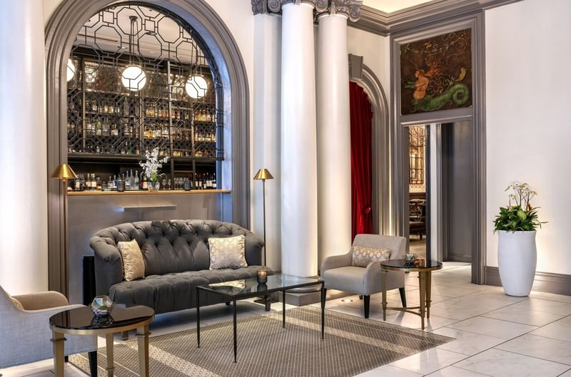 Tufted sofa by grey armchairs under white pillars near an arched bar area at Warwick San Francisco