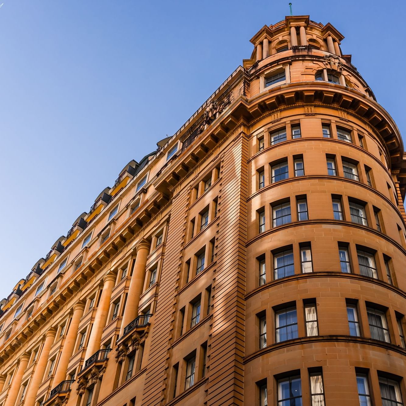 Impressive curved facade of the Paradox Sydney hotel building reaching toward a clear blue sky on a sunny day