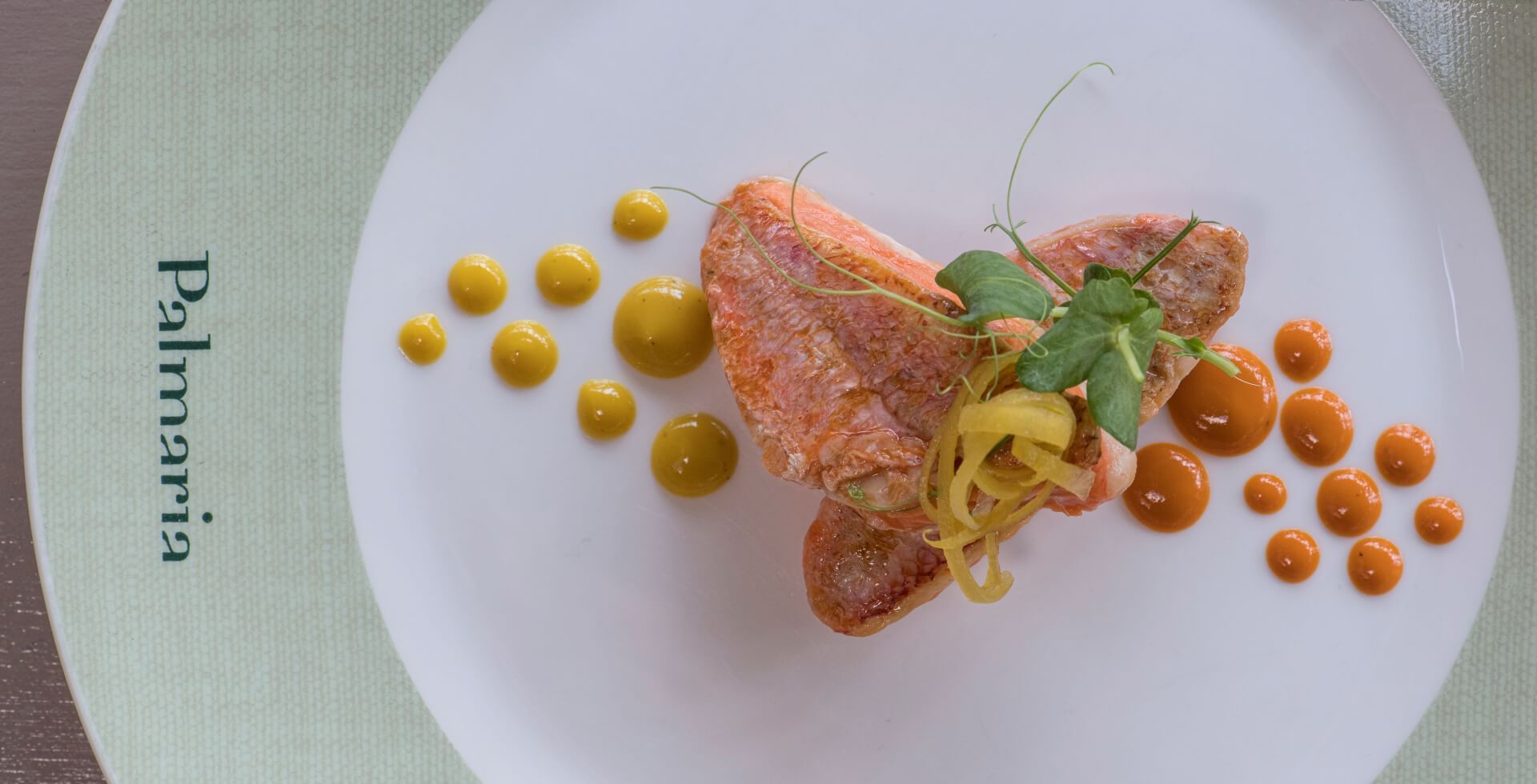 Plat de poisson avec sauce jaune et orange sur une assiette blanche de Palrmia.