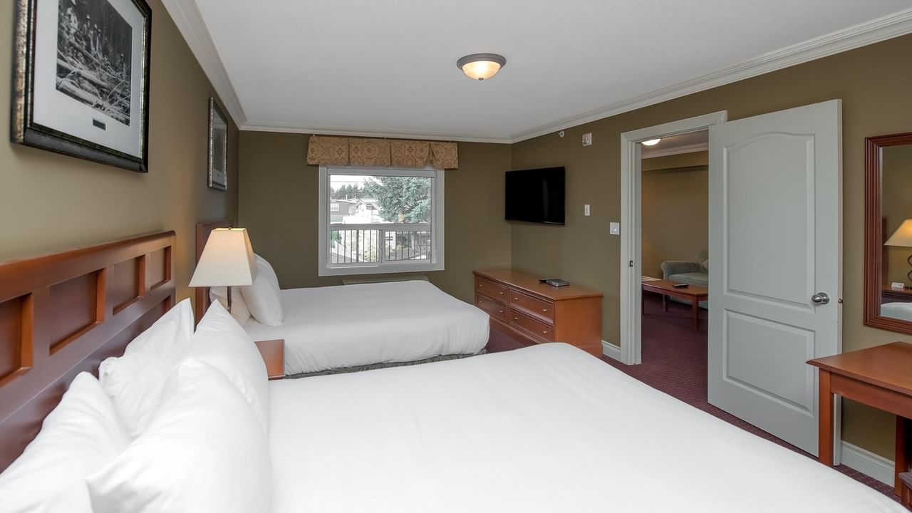 Spacious guest room with two beds, wooden furniture, and wall-mounted TV at Coast Edson Hotel