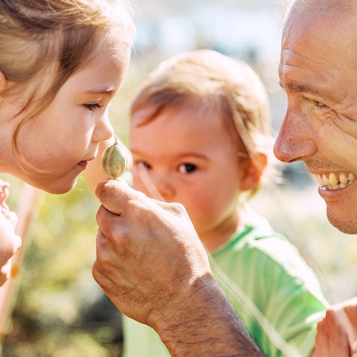Two kids and an adult smiling while examining a small seed at Falkensteiner Resort Lake Garda