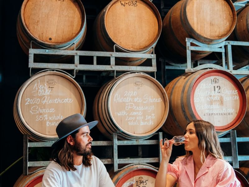 Two people tasting wine in front of stacked barrels at Fortitude Valley nearSofitel Brisbane Central