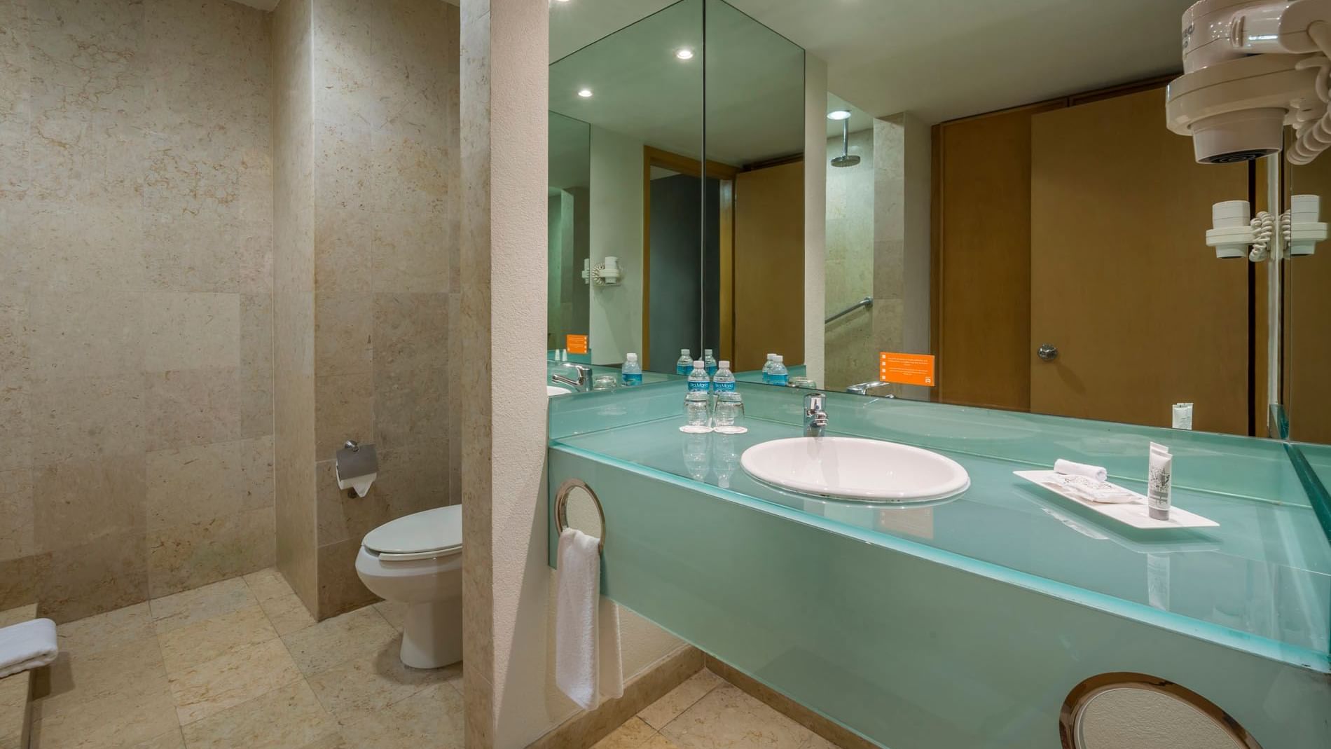 King Deluxe bathroom with a frosted glass vanity, large mirror, and neutral stone tiling at Real Inn Nuevo Laredo