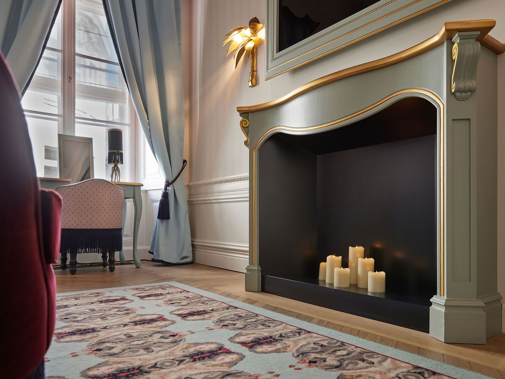 Elegant room with fireplace, decorative candles, chair, rug, and window with curtains on a sunny day.