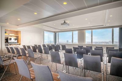 Conference room with rows of chairs & large windows overlooking a cityscape at The Hotels Brussels