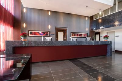 Lobby with red reception desk, pendant lights and abstract art on walls. at Sandman Signature Winnipeg Airport Hotel