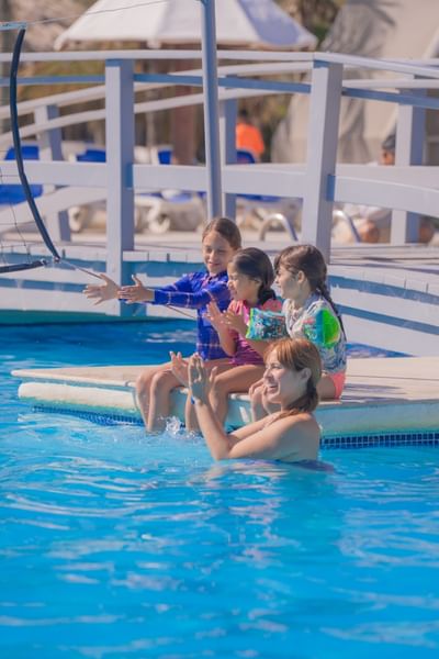 Mother and three children enjoying poolside activities with white cabana structure at Playa Blanca Beach Resort