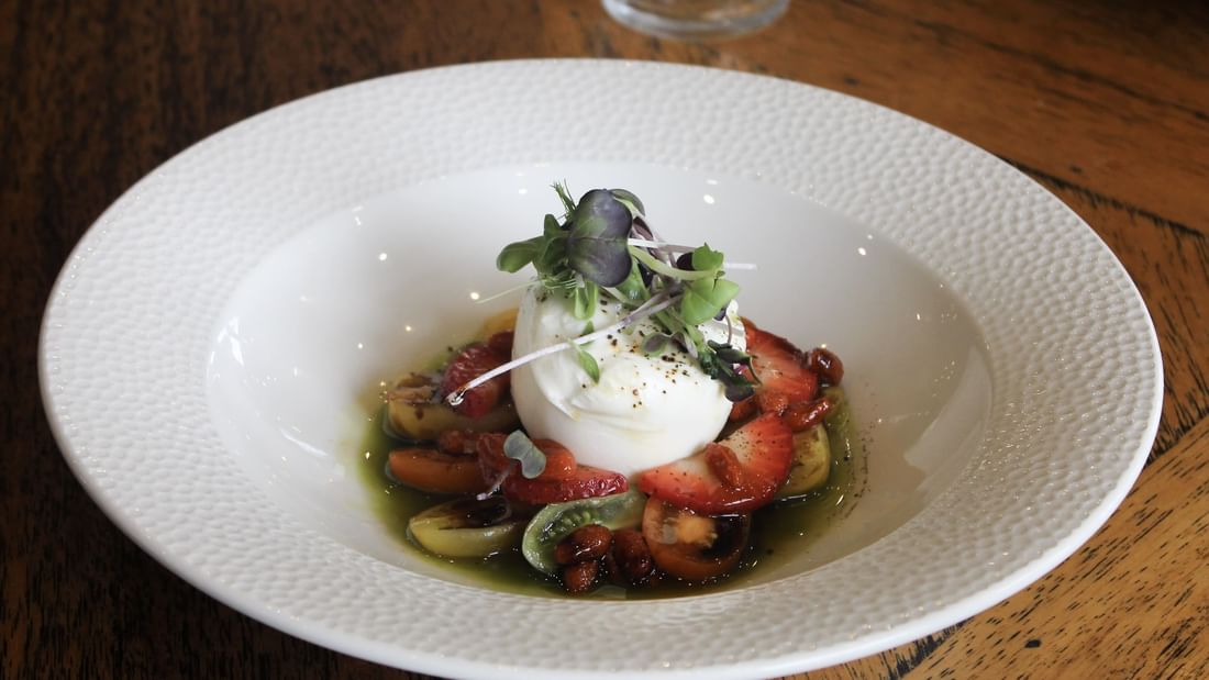 Plate of strawberries, burrata cheese, and greens from Karinya’s Refreshed Menu.