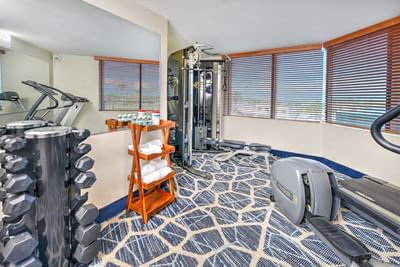 Daytona Bahama House Fitness Center with exercise machines, weight racks, and a rack of towels near large windows
