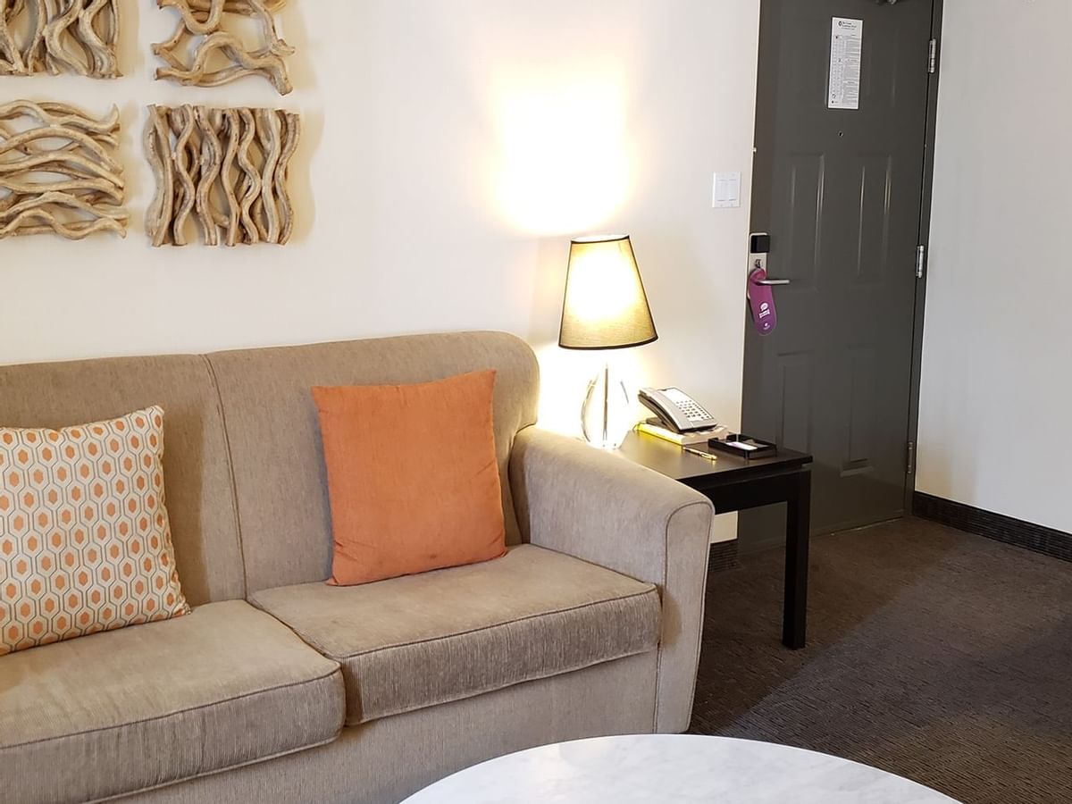 Living area of guest room with door, coffee table, couch, lamp