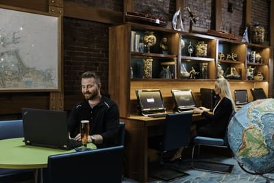 Man with a laptop and beer at a table and a woman at a computer in the business center at Harborside Inn Boston