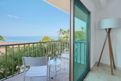 Balcony with ocean view, two white chairs, small table, and a lamp with a wooden base.