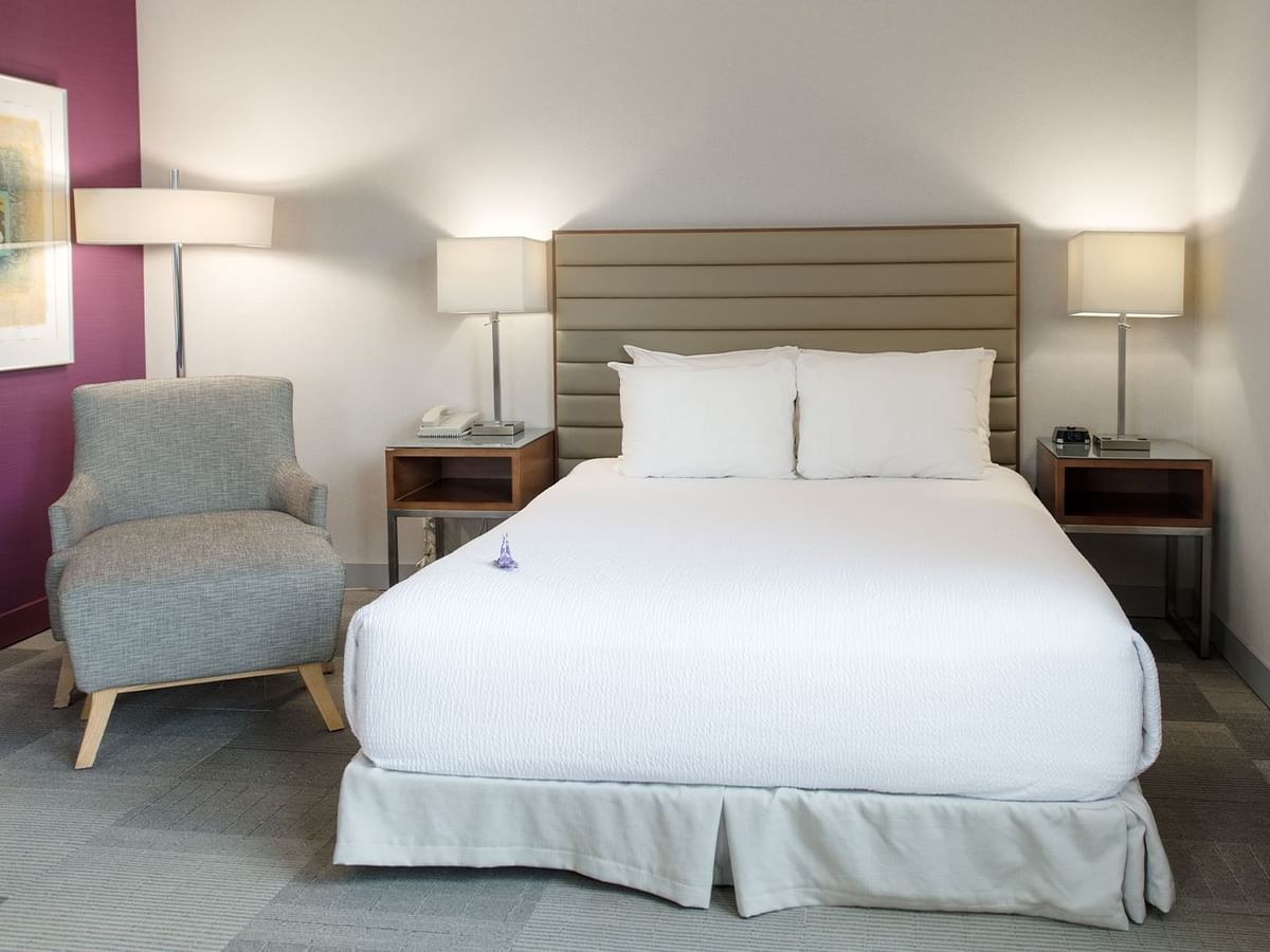 Accessible hotel room with a large bed, two nightstands with lamps, a chair, and artwork.