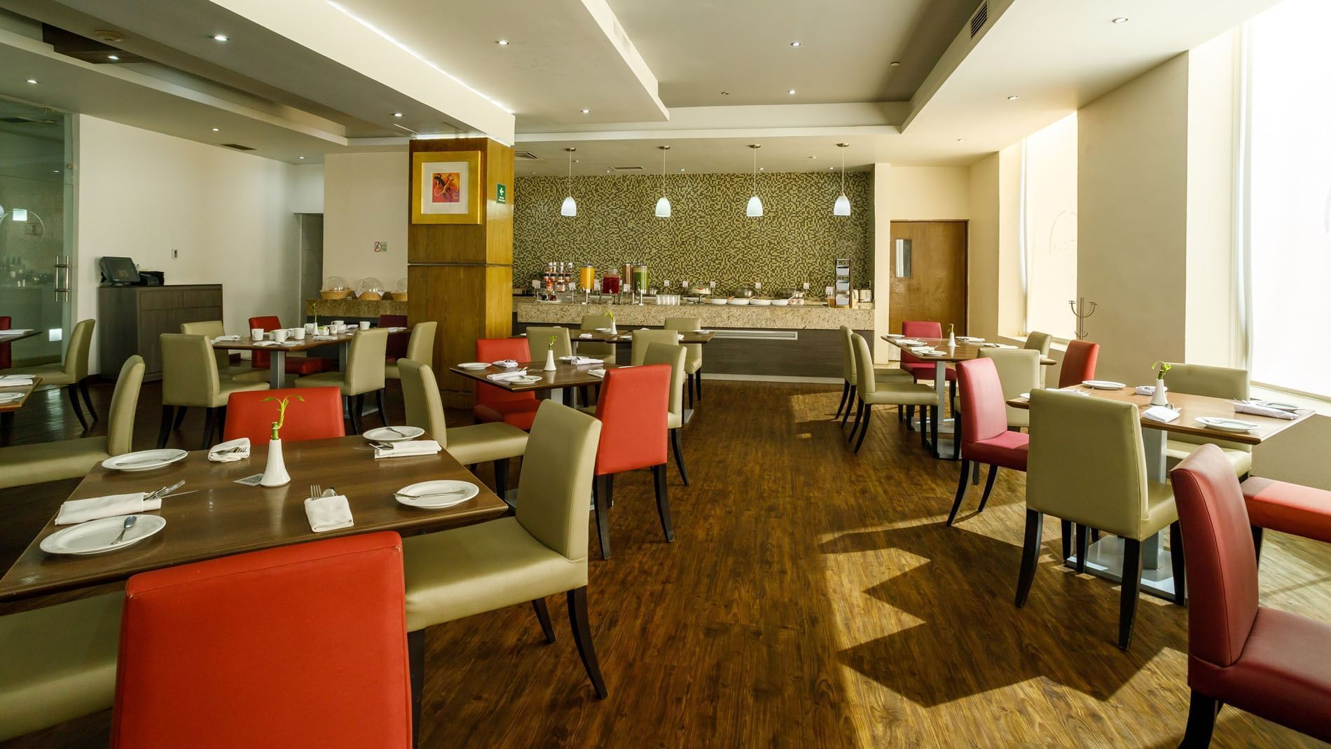 Stock Café dining room featuring red and tan chairs, wooden tables, and a breakfast buffet bar at Real Inn Torreon