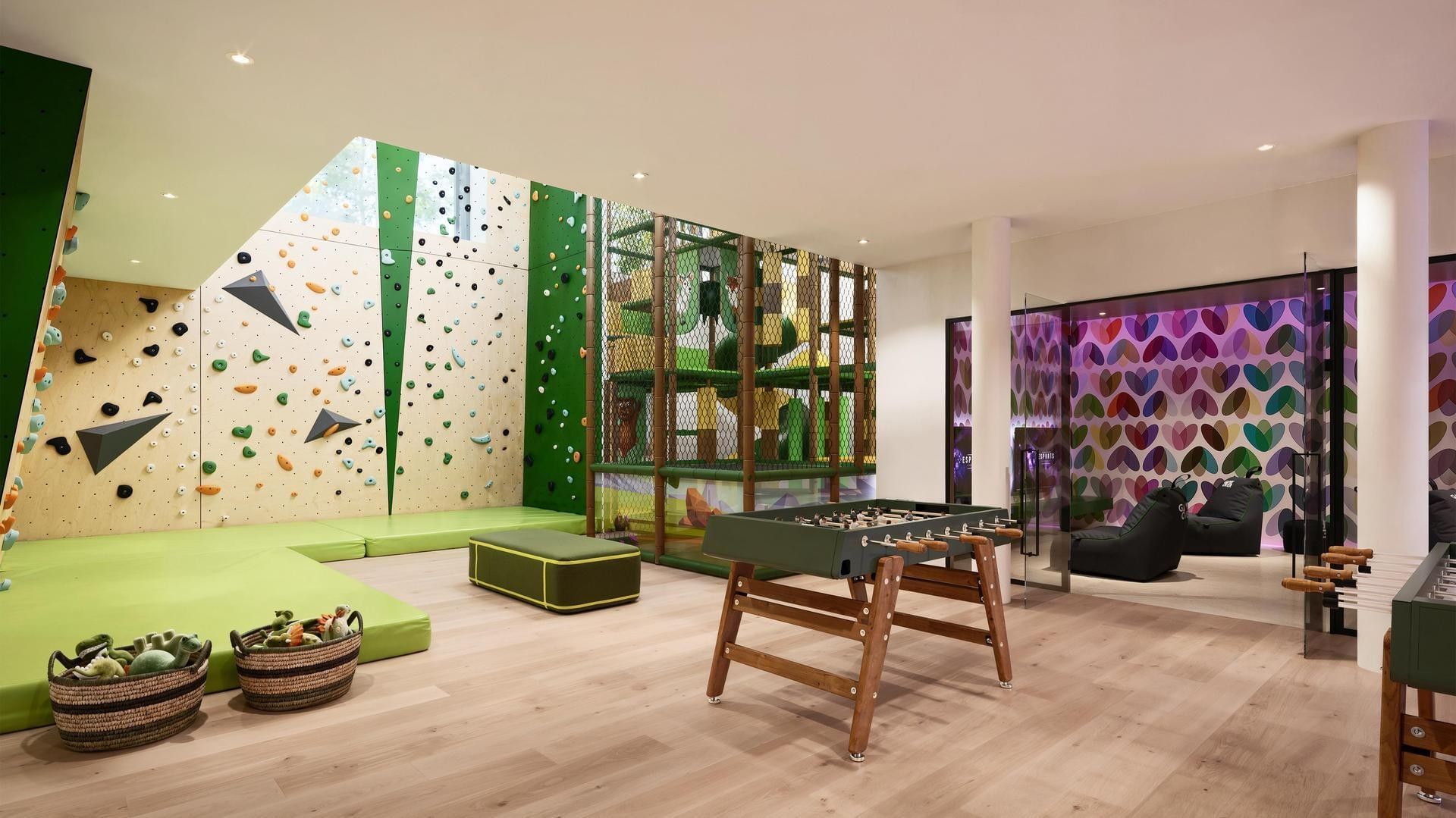 Bright playroom with climbing walls, a green foosball table, and colorful seating areas.