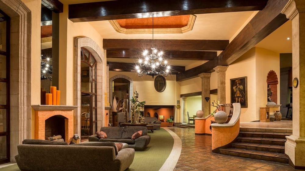 Warmly lit lobby showing a stone fireplace, grand stairs, and rustic wooden beams at Quinta Real Zacatecas