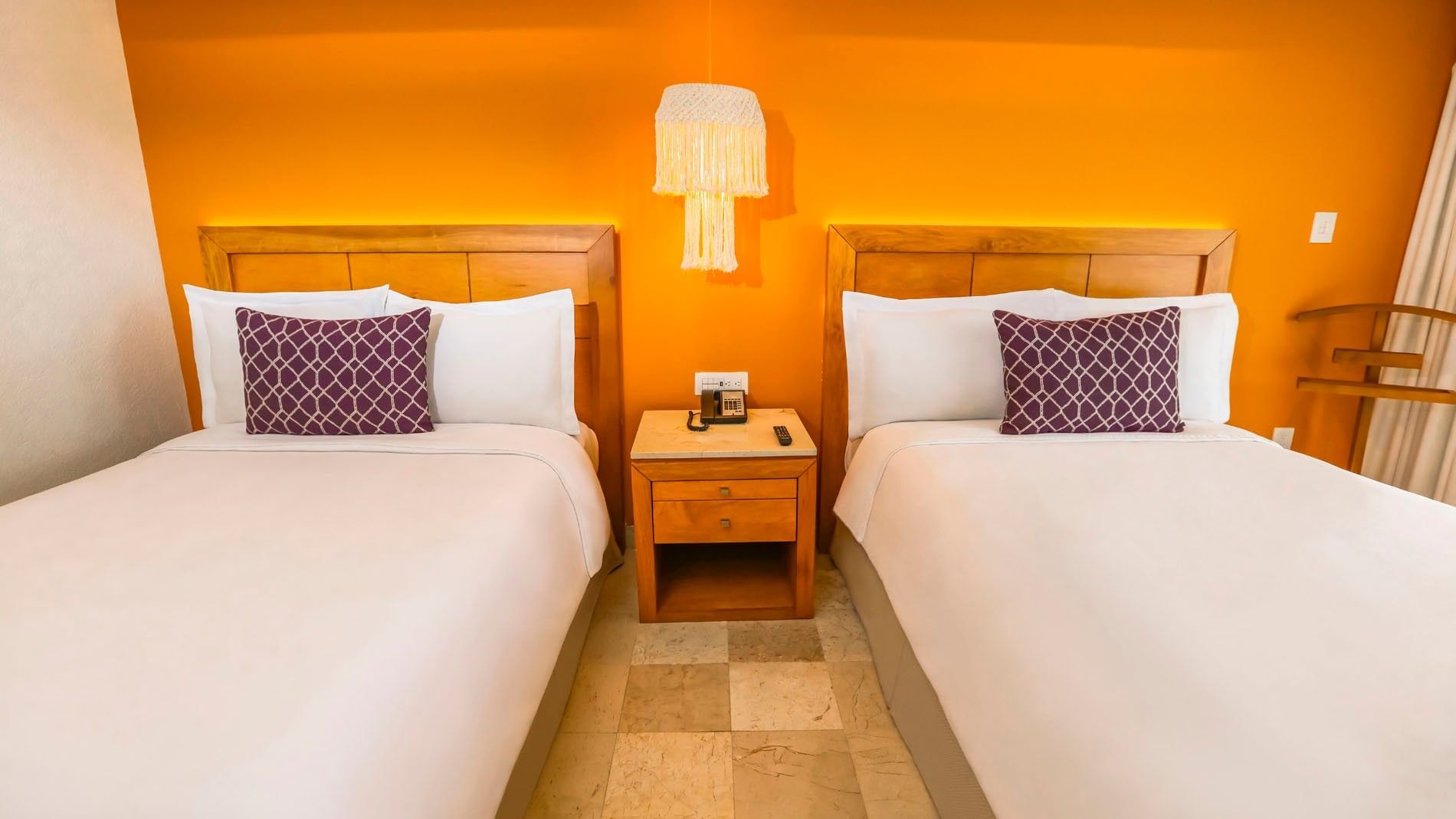 Double beds in 2 Double Deluxe Superior with a shared nightstand against a vibrant orange backdrop at Camino Real Veracruz