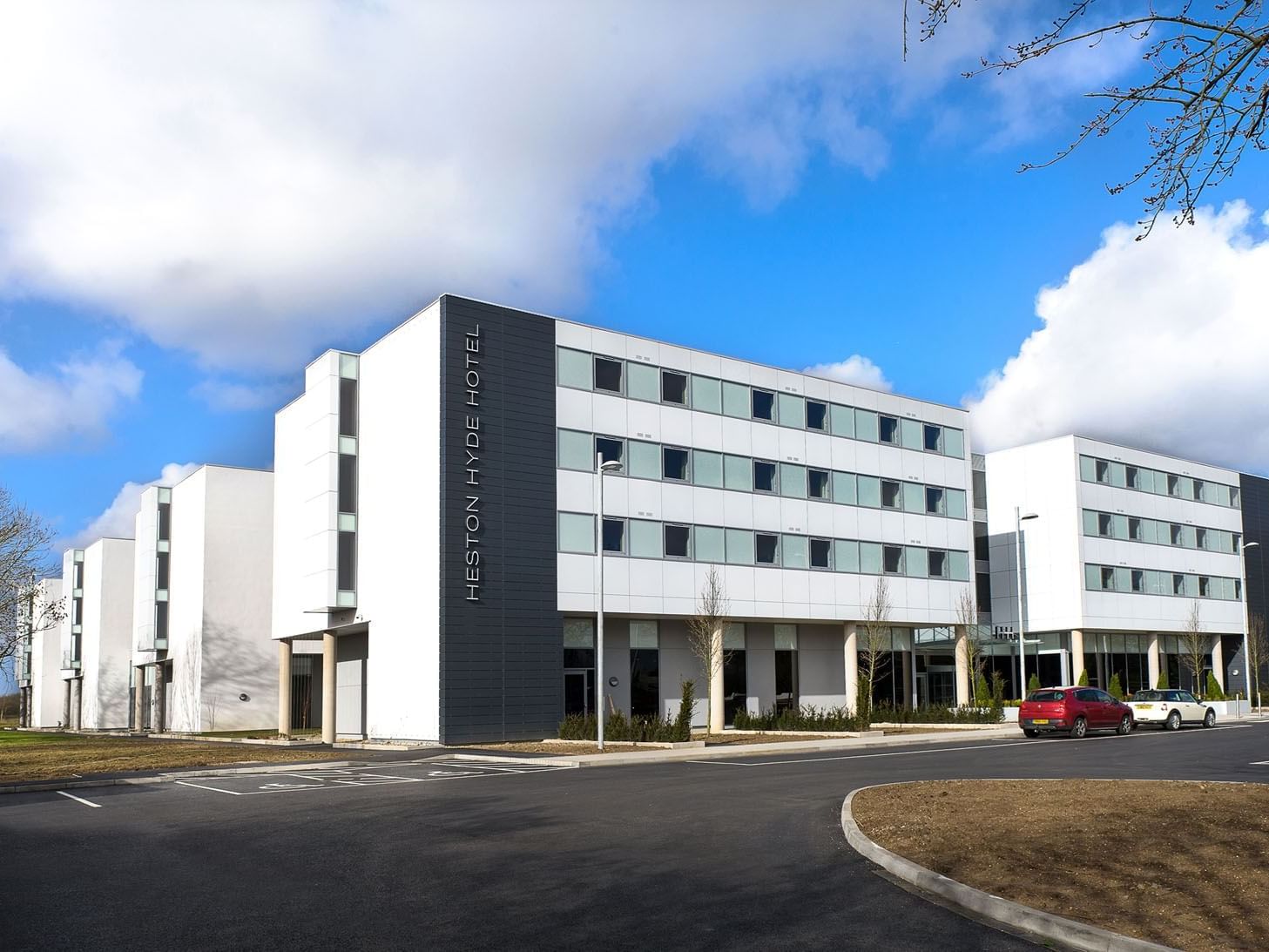 Exterior of Heston Hyde Hotel featuring modern architecture with large windows and a parking area