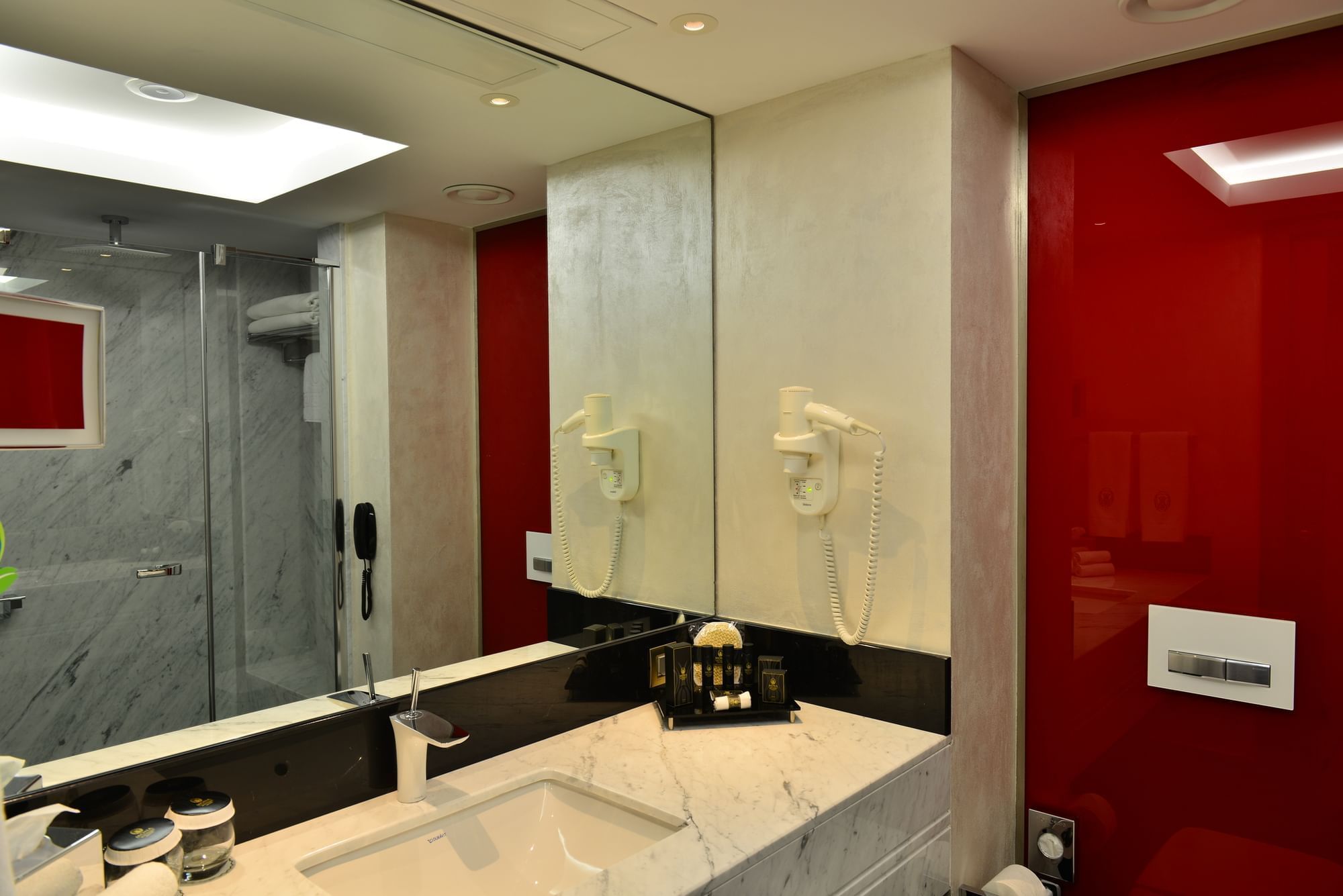 Marble sink by a vibrant red wall under a large mirror in Junior Suite at Warwick Ankara